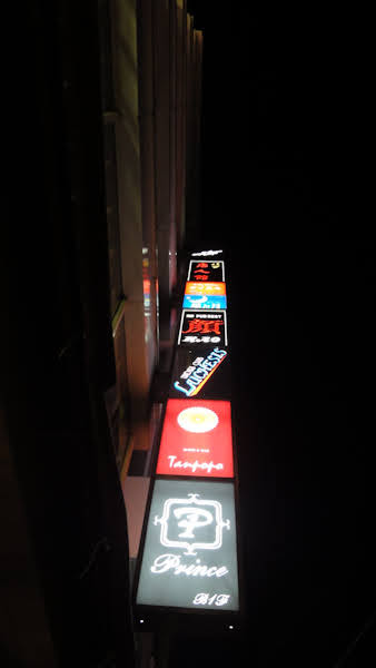 small signs in a vertical stack show the many small bars within one building